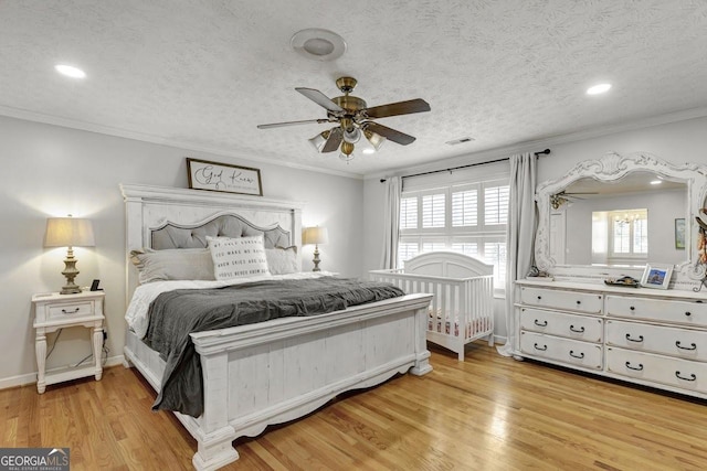 bedroom featuring light wood-style floors, a textured ceiling, visible vents, and crown molding