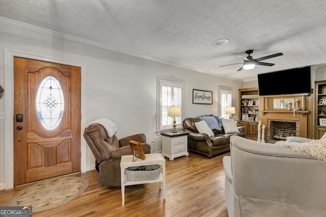 living area with light wood-style floors, ornamental molding, a brick fireplace, ceiling fan, and a textured ceiling