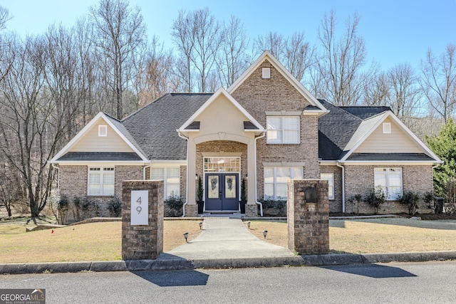 view of front of property with french doors, brick siding, a front lawn, and roof with shingles