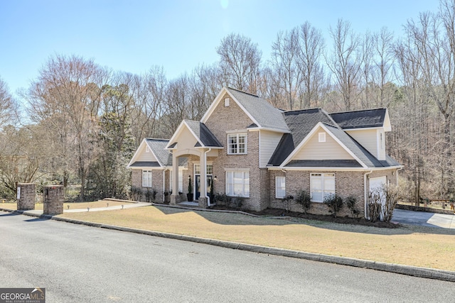 traditional-style home featuring a shingled roof, a front lawn, and brick siding