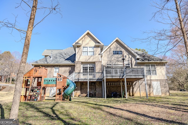 rear view of house featuring a deck, a playground, brick siding, a shingled roof, and a yard