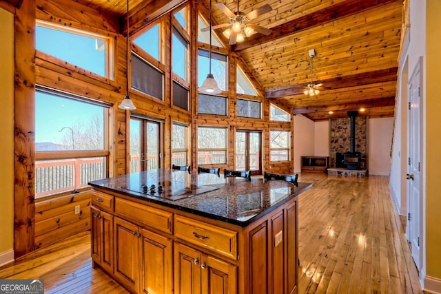 kitchen featuring light wood-style floors, a wood stove, ceiling fan, beamed ceiling, and black electric cooktop