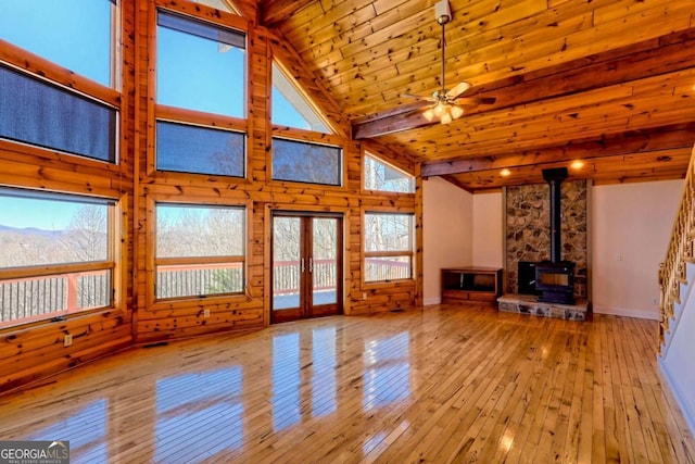 unfurnished living room with french doors, beam ceiling, wood-type flooring, a wood stove, and high vaulted ceiling