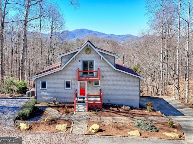 view of front of home with driveway, a balcony, central AC, a mountain view, and a wooded view