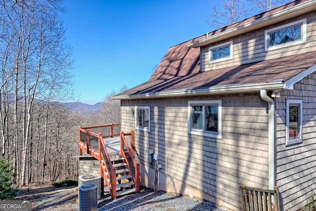 view of side of home with stairs, a shingled roof, and cooling unit