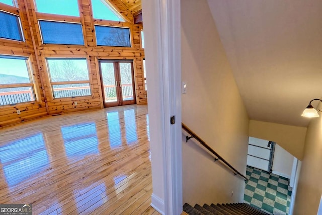 stairs featuring high vaulted ceiling, hardwood / wood-style floors, wood walls, and french doors