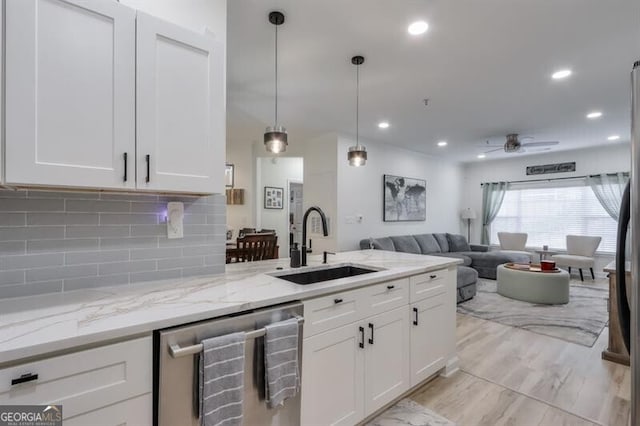 kitchen featuring tasteful backsplash, open floor plan, stainless steel dishwasher, white cabinetry, and a sink