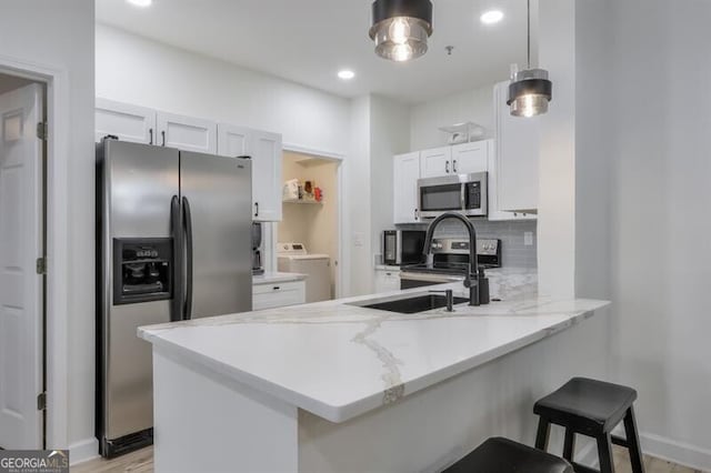 kitchen featuring a breakfast bar area, appliances with stainless steel finishes, washer / clothes dryer, a peninsula, and backsplash