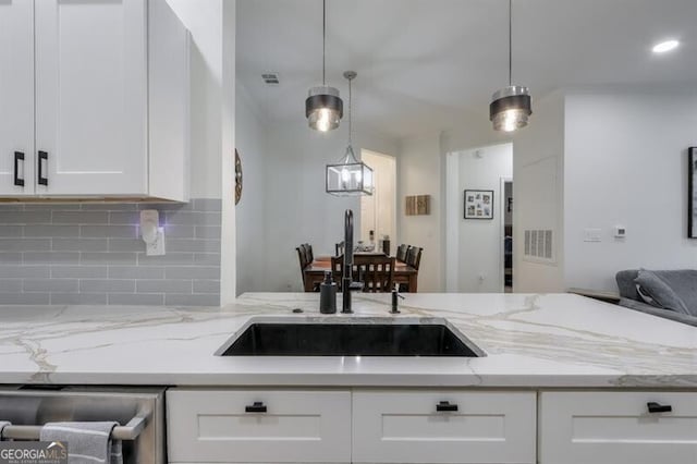 kitchen with visible vents, light stone counters, a sink, white cabinetry, and backsplash