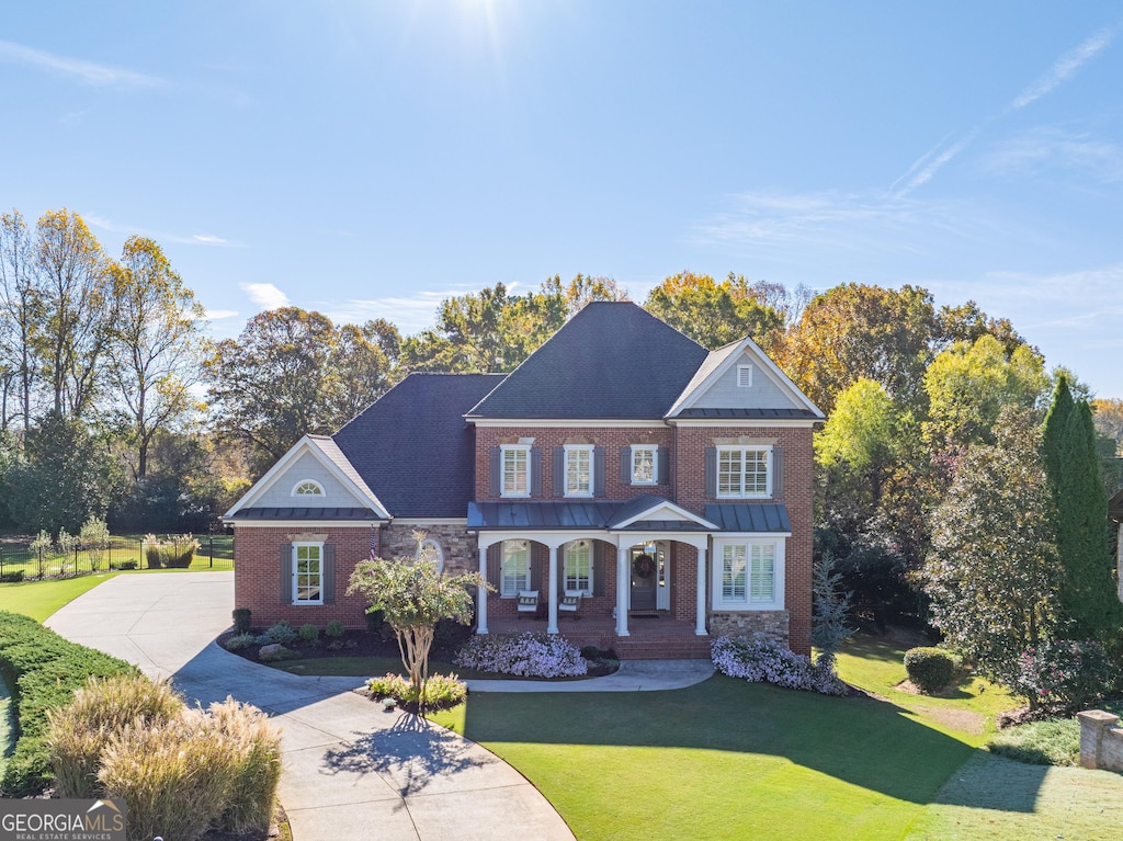 view of front facade featuring driveway, a standing seam roof, a front lawn, a porch, and brick siding