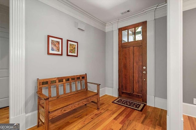 foyer featuring baseboards, visible vents, wood finished floors, and ornamental molding