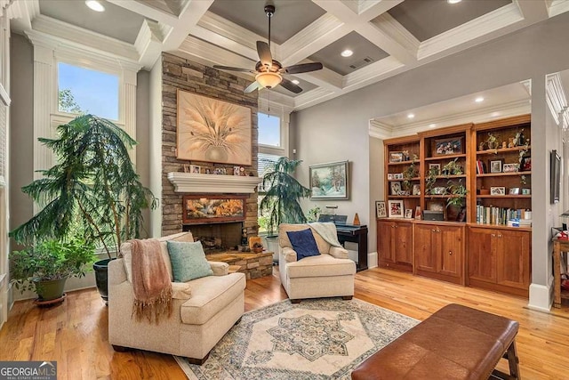 living area featuring light wood-style flooring, beam ceiling, coffered ceiling, and a stone fireplace