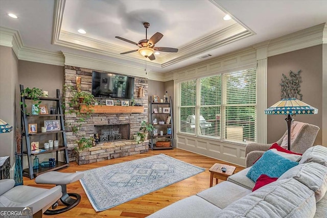 living area with ceiling fan, a tray ceiling, wood finished floors, and a stone fireplace