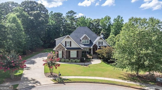 craftsman house with driveway, stone siding, a chimney, and a front yard