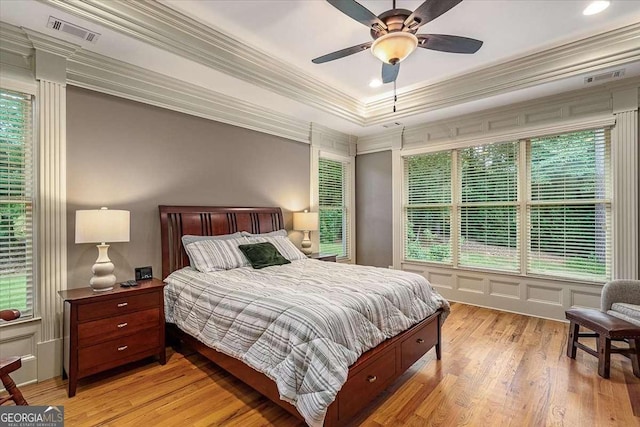 bedroom with ornamental molding, visible vents, a decorative wall, and light wood-style flooring