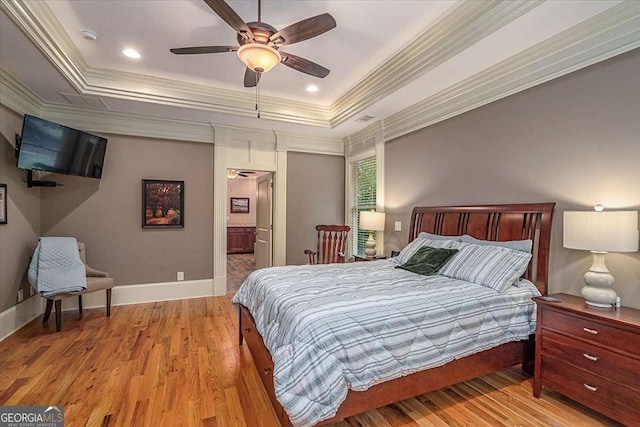 bedroom with light wood-style flooring, baseboards, a raised ceiling, and crown molding