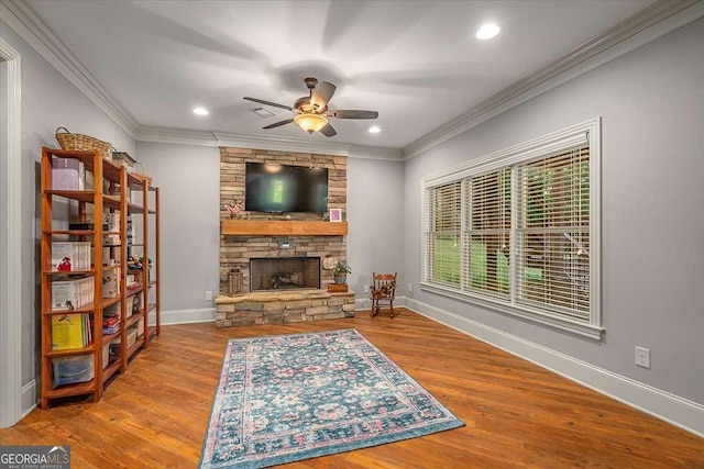 living room featuring baseboards, a stone fireplace, wood finished floors, and crown molding