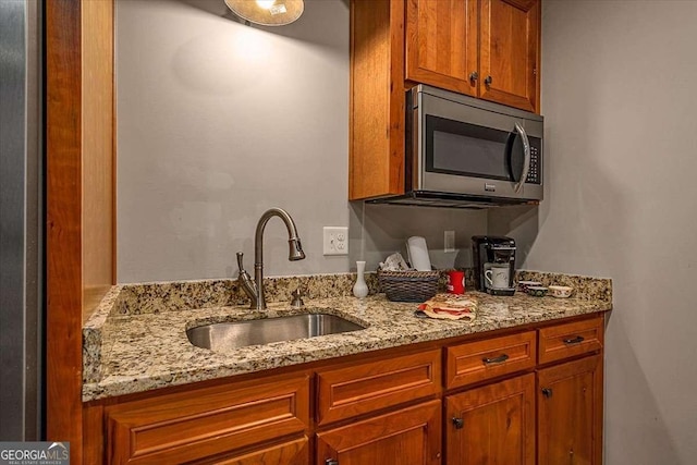 kitchen with light stone counters, stainless steel microwave, a sink, and brown cabinets