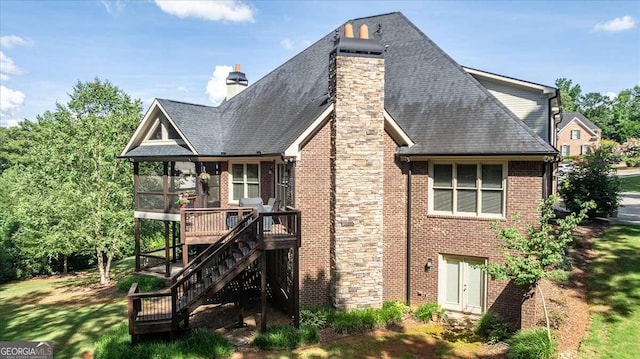 rear view of house with brick siding, a sunroom, stairway, a wooden deck, and a chimney