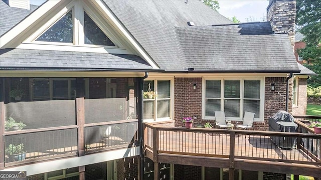 back of house featuring brick siding, a chimney, a shingled roof, and a sunroom