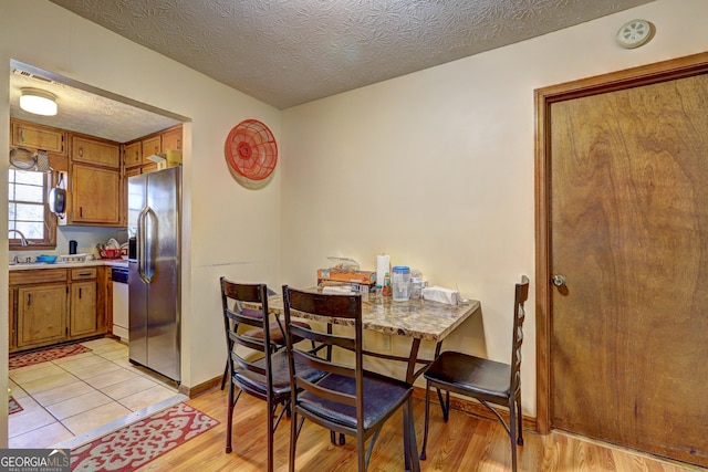 dining space featuring a textured ceiling, light wood-style flooring, and baseboards