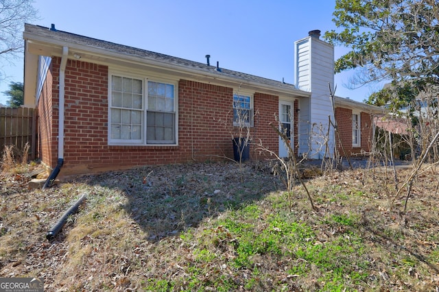 back of house featuring a chimney, fence, and brick siding