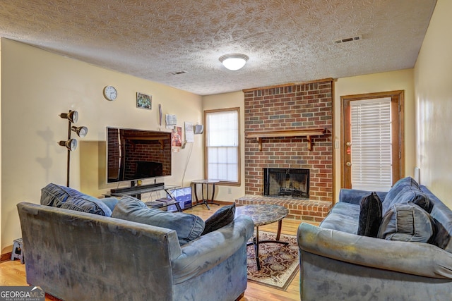 living area with light wood finished floors, baseboards, visible vents, a textured ceiling, and a fireplace