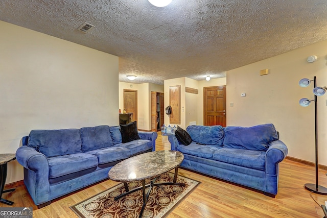 living area featuring baseboards, a textured ceiling, visible vents, and wood finished floors