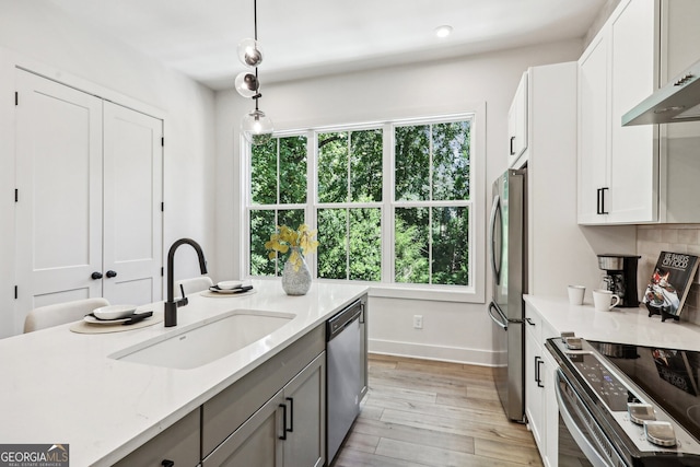 kitchen featuring light wood-style flooring, stainless steel appliances, pendant lighting, a sink, and exhaust hood