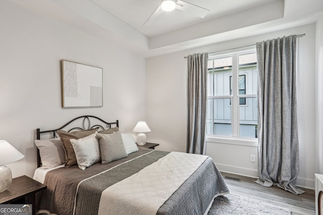 bedroom with baseboards, visible vents, a ceiling fan, a raised ceiling, and wood finished floors