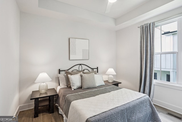 bedroom with a raised ceiling, wood finished floors, visible vents, and baseboards