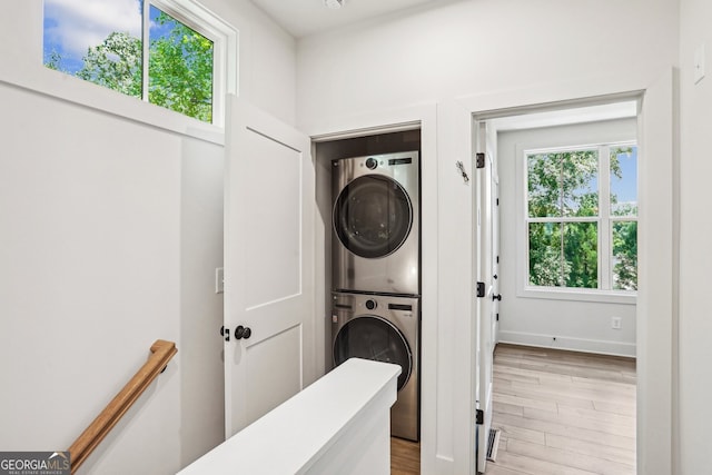 clothes washing area featuring light wood-style floors, laundry area, baseboards, and stacked washing maching and dryer