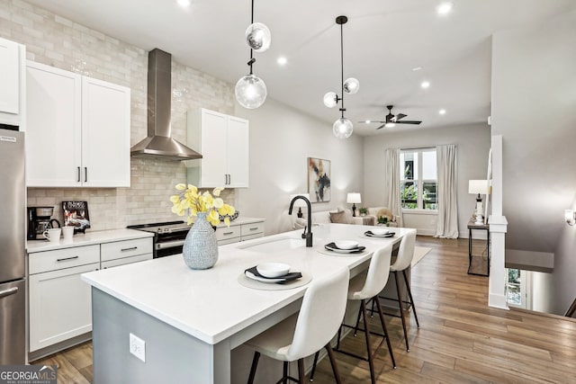 kitchen featuring stainless steel appliances, backsplash, a sink, wall chimney range hood, and an island with sink