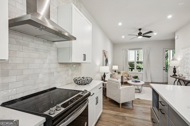 kitchen with open floor plan, light countertops, wall chimney range hood, and black range with electric cooktop