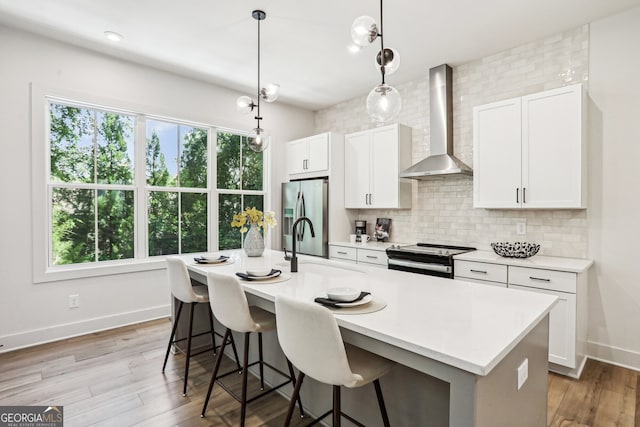 kitchen featuring an island with sink, stainless steel appliances, light countertops, wall chimney range hood, and backsplash