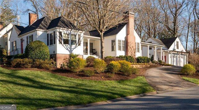 view of front facade with driveway, a chimney, an attached garage, a front lawn, and brick siding