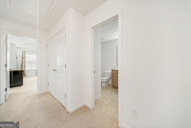 hallway featuring baseboards, attic access, and light colored carpet