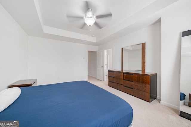 carpeted bedroom with a tray ceiling, a ceiling fan, and baseboards