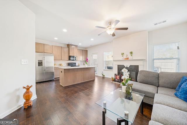 living room with visible vents, dark wood finished floors, baseboards, a glass covered fireplace, and ceiling fan