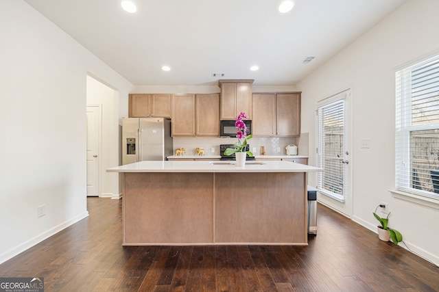 kitchen featuring black microwave, a kitchen island, light countertops, stainless steel fridge with ice dispenser, and dark wood-style floors