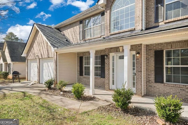 property entrance with a garage, driveway, a shingled roof, a porch, and brick siding