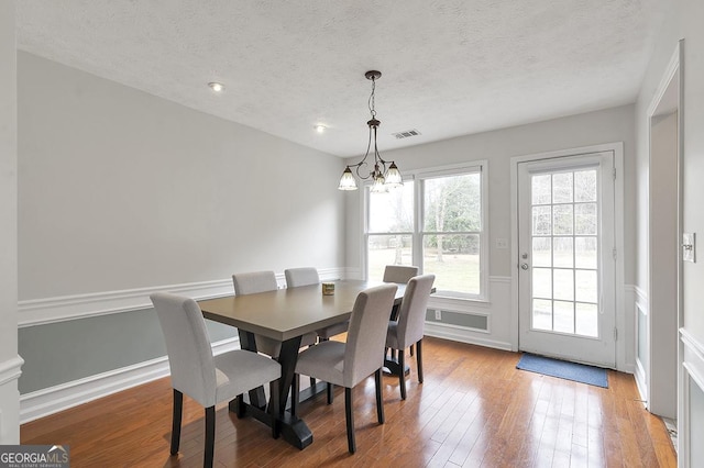 dining space with visible vents, wainscoting, hardwood / wood-style floors, an inviting chandelier, and a textured ceiling