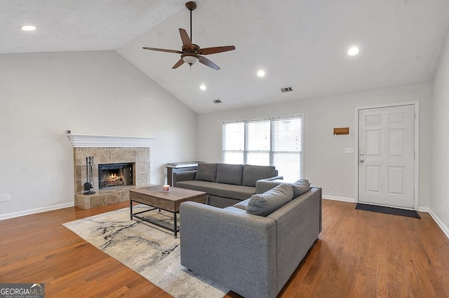 living area featuring baseboards, visible vents, a tile fireplace, lofted ceiling, and wood finished floors