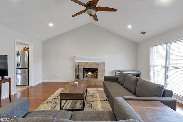 living area with lofted ceiling, visible vents, wood finished floors, a tile fireplace, and baseboards