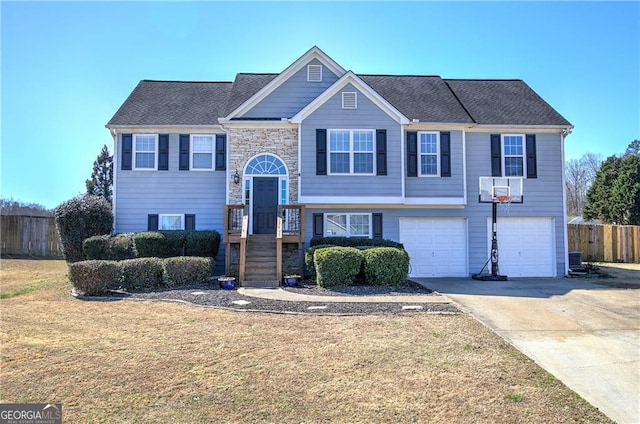 bi-level home with an attached garage, fence, driveway, stone siding, and a front lawn