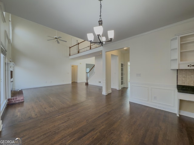 unfurnished living room featuring ceiling fan with notable chandelier, a high ceiling, dark wood-style flooring, ornamental molding, and stairway