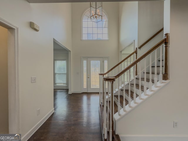 entryway featuring baseboards, a towering ceiling, stairway, wood finished floors, and an inviting chandelier