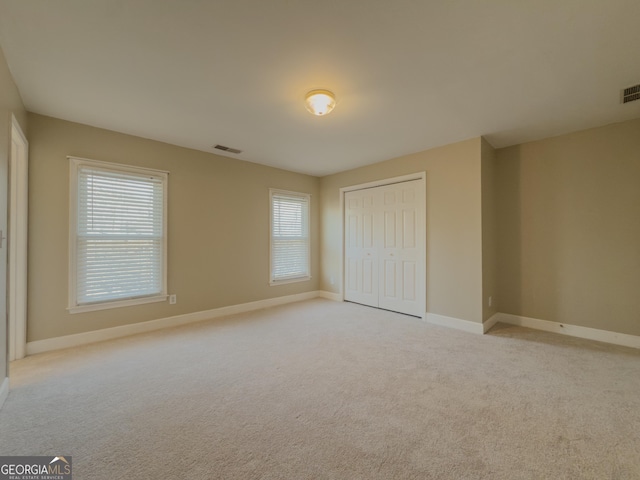 unfurnished bedroom with light colored carpet, a closet, visible vents, and baseboards