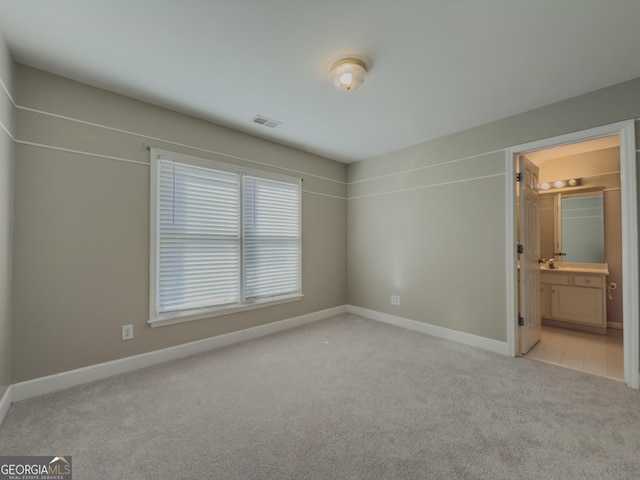 unfurnished bedroom featuring light colored carpet, connected bathroom, visible vents, and baseboards