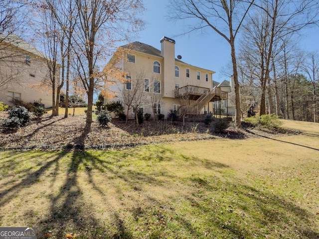 back of house featuring a deck, a chimney, a lawn, and stairway